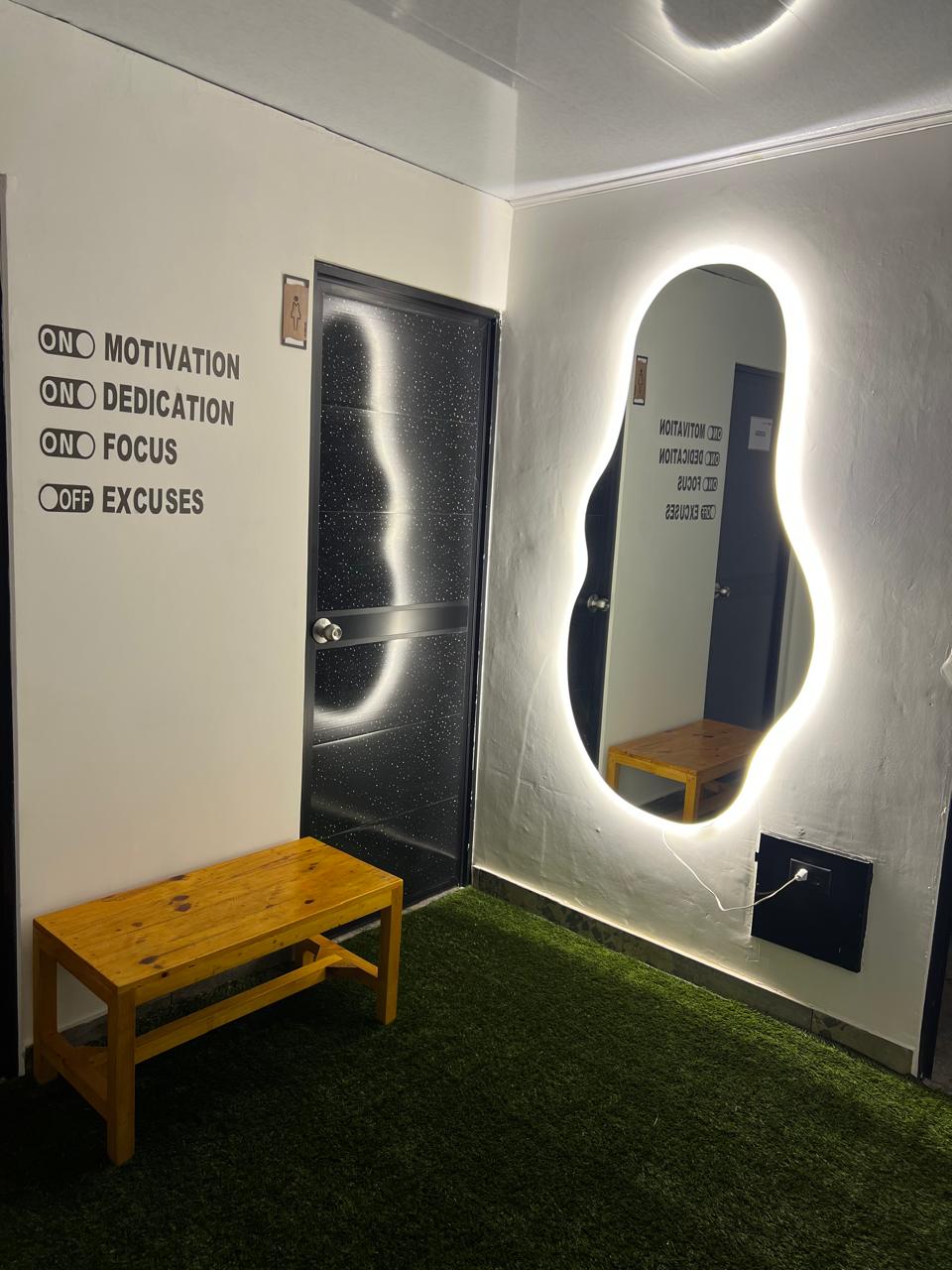 Zona de vestier con banca de madera, espejo iluminado y baño