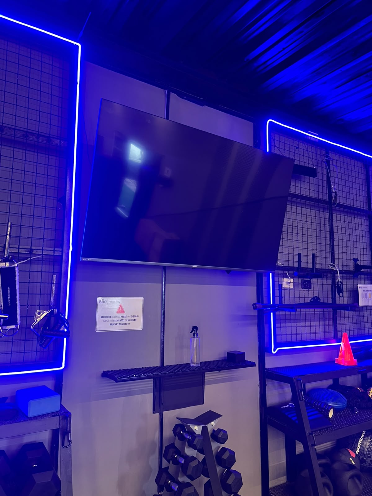 Pantalla y paneles de neón sobre el rack de mancuernas